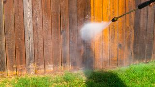 A pressure washer cleaning a wooden fence with a grassy lawn in front