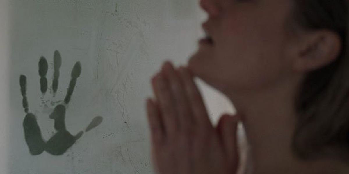 Cecilia (Elisabeth Moss) stands in the shower as a handprint appears on the foggy door in the backgr