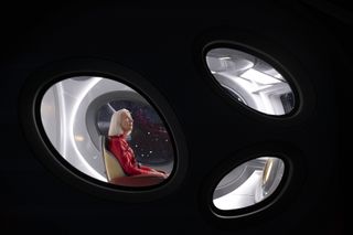 Solos: Peg, played by Helen Mirren, sits inside a spacecraft wearing a red jumpsuit. The camera is outside, looking in through three egg-shaped windows