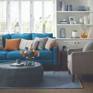 A living room with a blue sofa and white built-in shelving contrasted by orange accessories