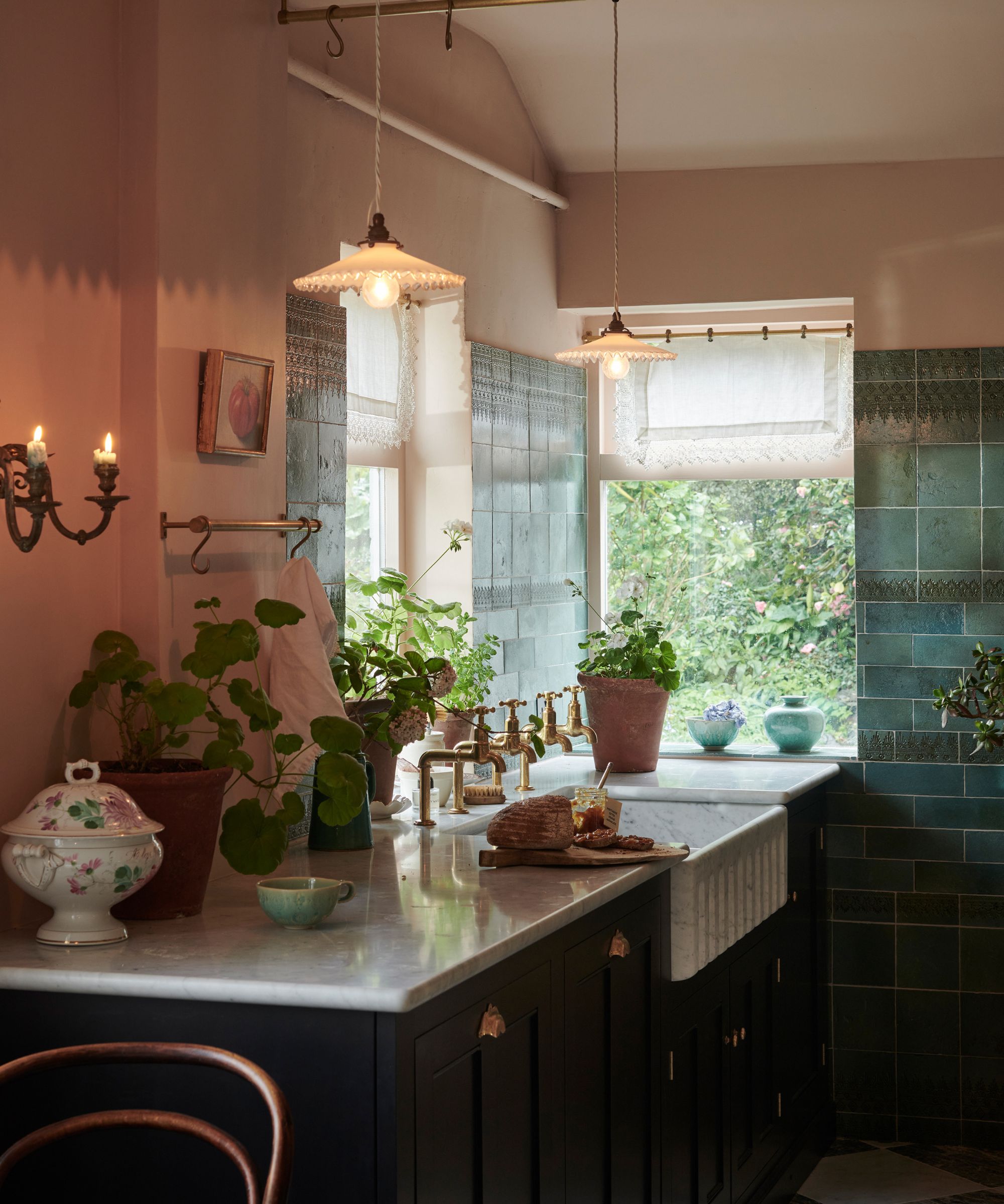 A cozy kitchen with pink walls, green cabinets, and wall sconces for candles