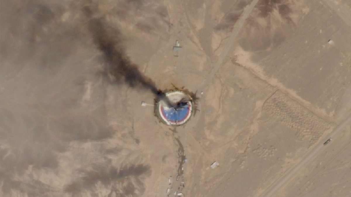 satellite photo of a circular, blue launch pad in the desert with black smoke rising from it