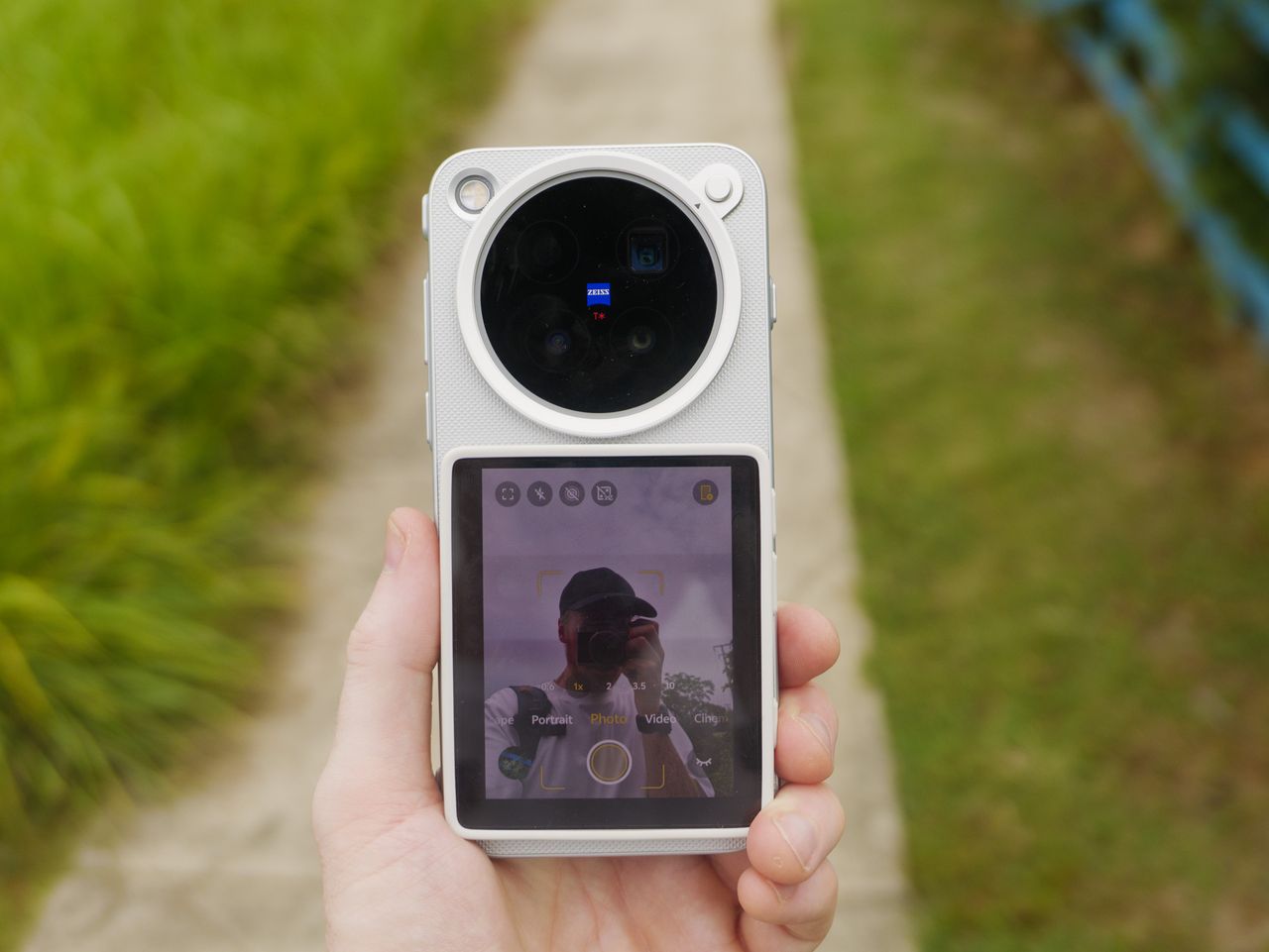 The Vivo X500 Pro Max phone in user's hand, in its dedicated case for magnetic accessories, with Vivo's selfie screen attached, and person is vlogging by a lake