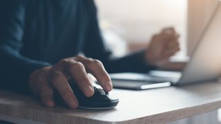 A man clicking on a mouse while browsing the web on his laptop