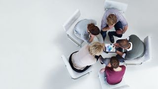 Top down photo of work colleagues sat in a circle while looking at a tablet