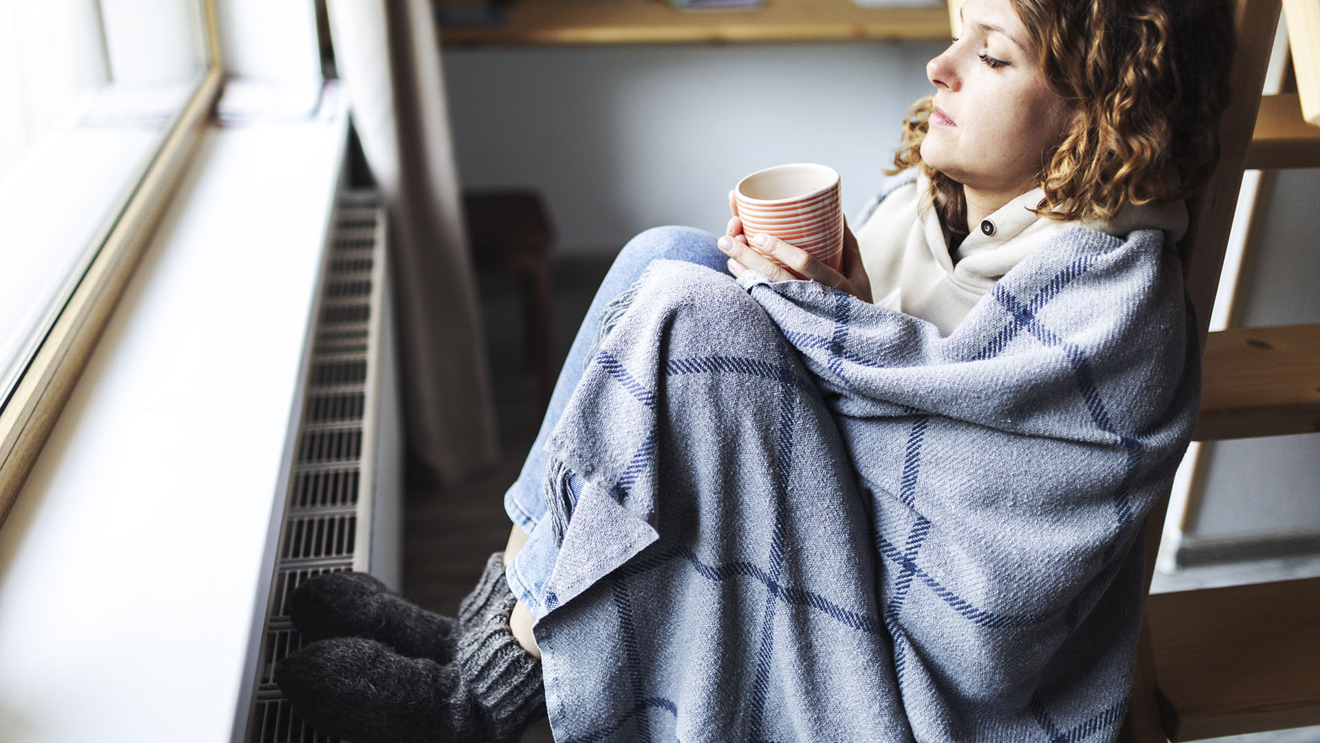 Woman wrapped in blanket, with feet against the radiator