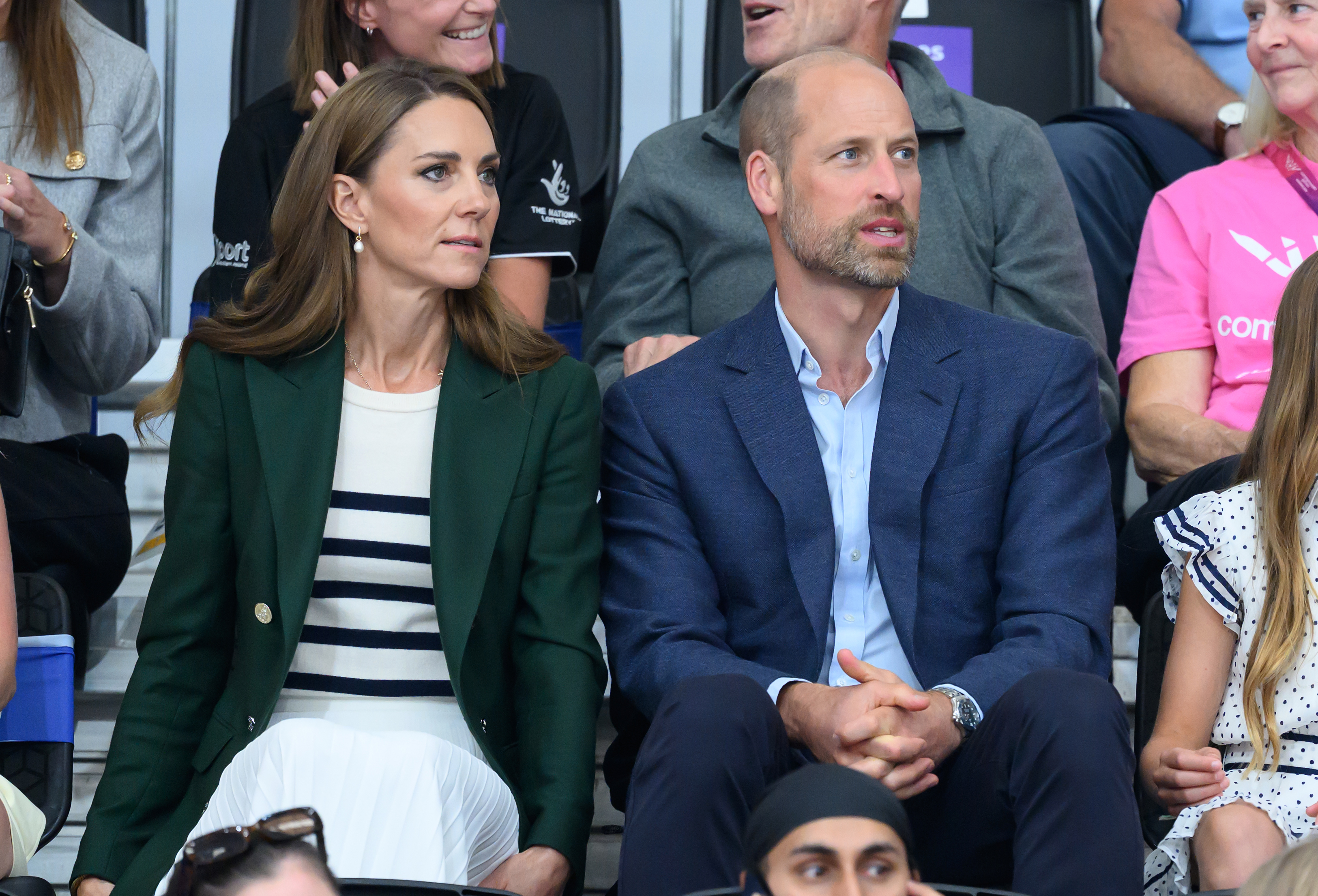 Princess Kate wears a green blazer a Breton striped top and Prince William has a bald head and wears a navy suit