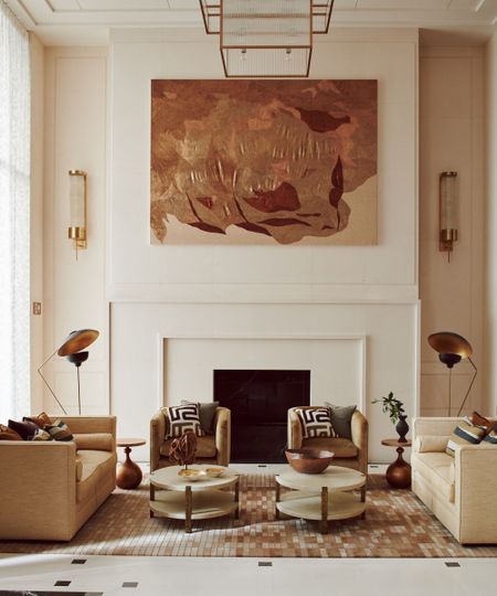 Symmetrically arranged, elegant living room with neutral-toned seating, a central fireplace, and a large, textured copper-toned artwork above the mantel