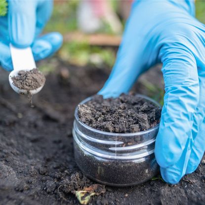 Gloved hands place soil sample into small jar using small spoon