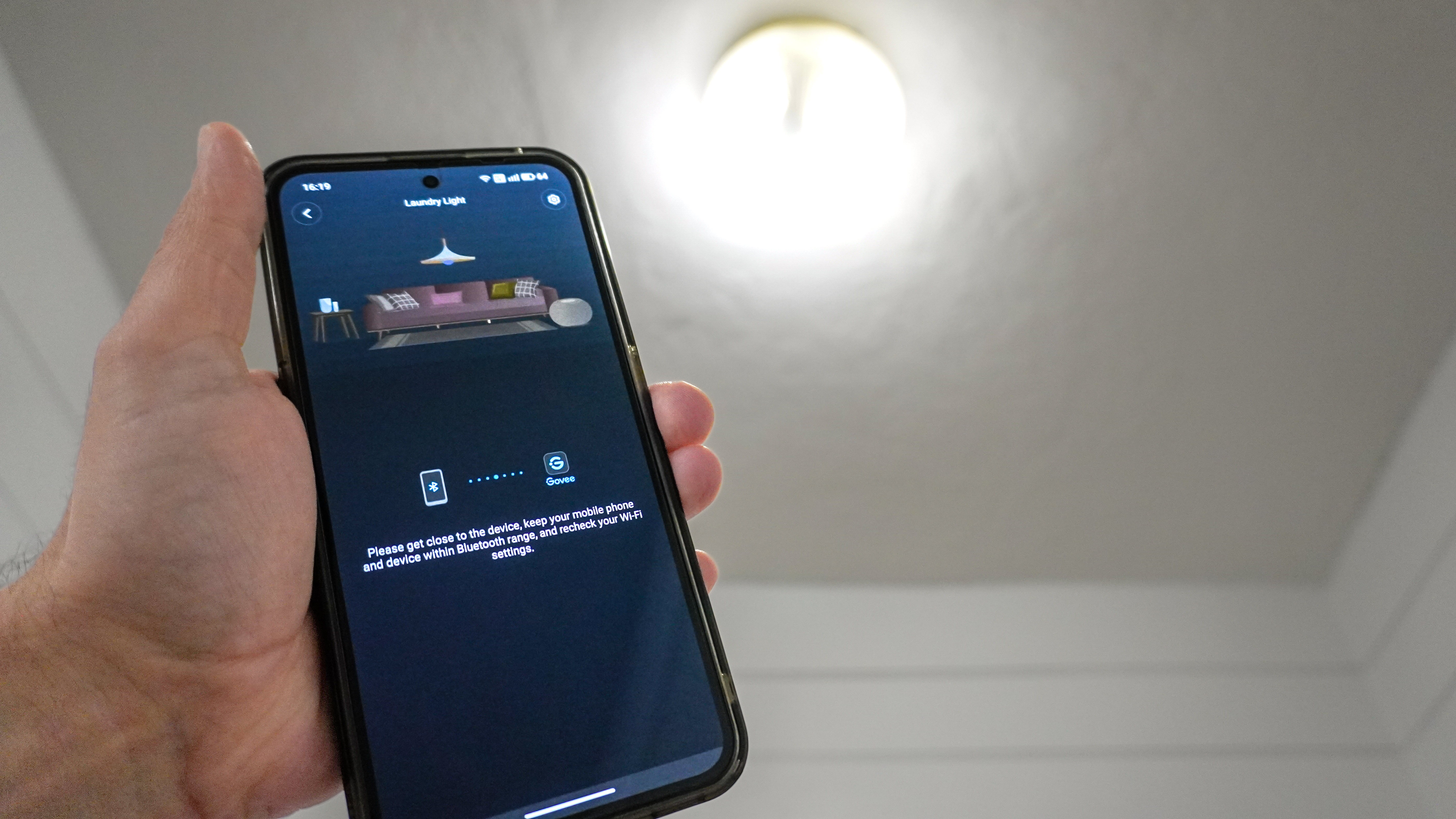 A person holding a phone with the Govee app showing the dreaded Bluetooth reconnection screen in front of a Govee smart light