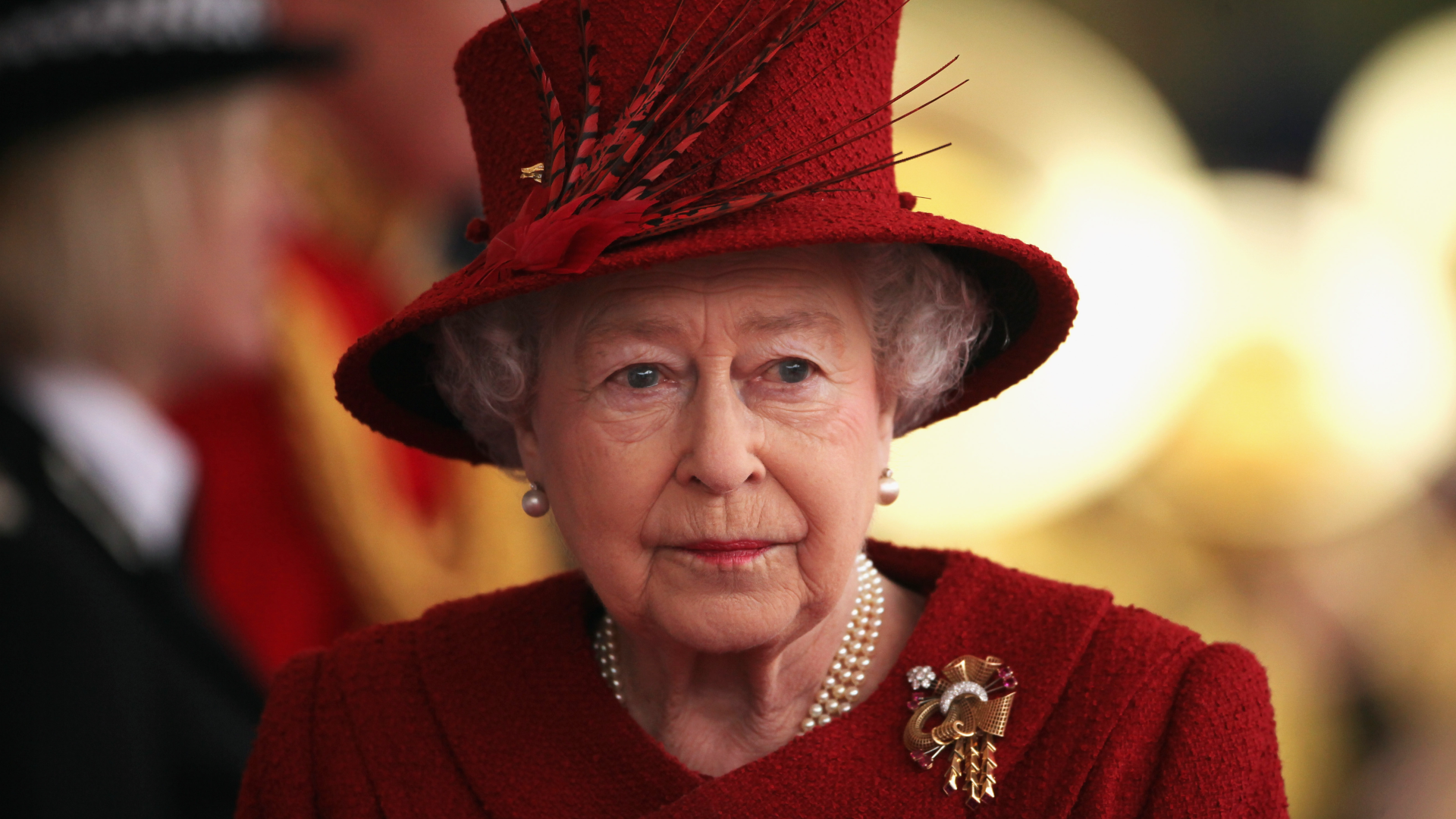 Queen Elizabeth wears a scarlet coat and matching hat with feathers in it and looks tearful