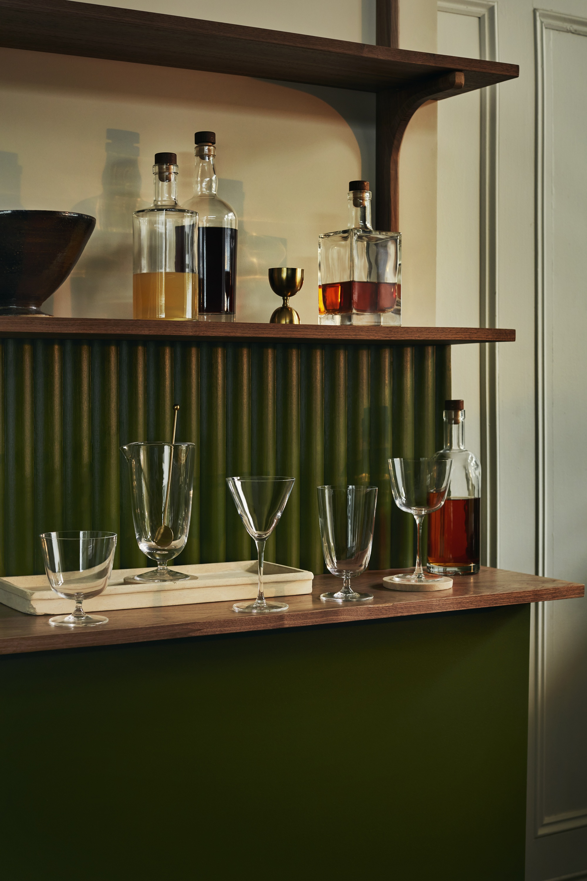 various cocktail glasses on a green home bar with bottles of liquor
