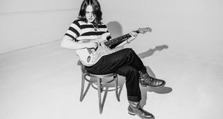 A black and white image of Tyler Bryant sitting, playing his Pinky Strat