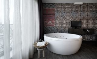 Bathroom with large bath and table, Curtain cover large window and wallpapered wall, wooden floors