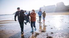 A family group walking on beach in winter, with grandparents swinging grandchild in front, and small child on father's shoulders, with mother alongside, in the background