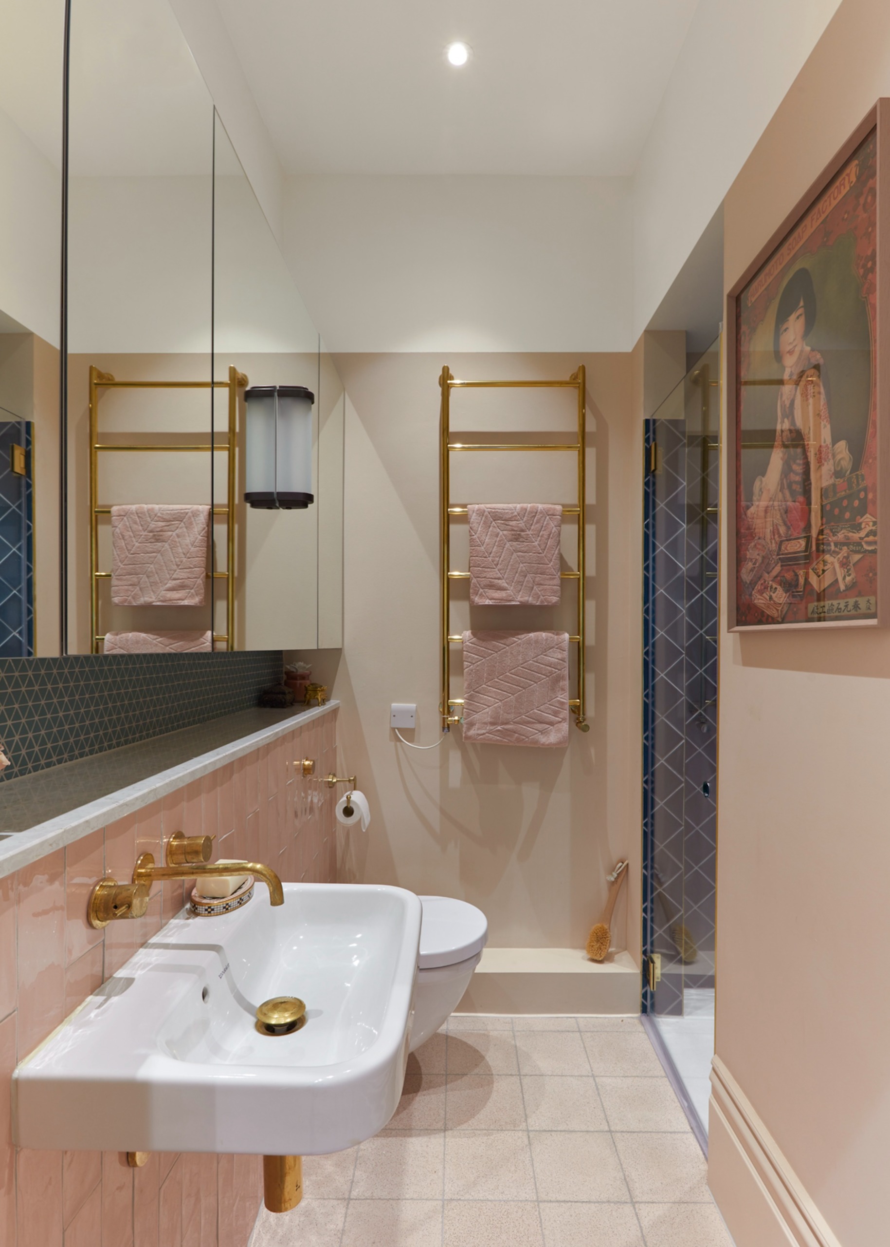 a narrow bathroom with pale pink neutral walls, a wall hung basin and gold heated towel rail
