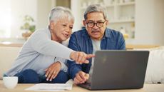 An older couple look at a laptop while sitting on their living room sofa.