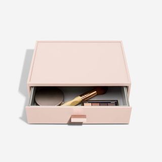 A pink rectangular makeup organizer has a drawer partially open with makeup inside