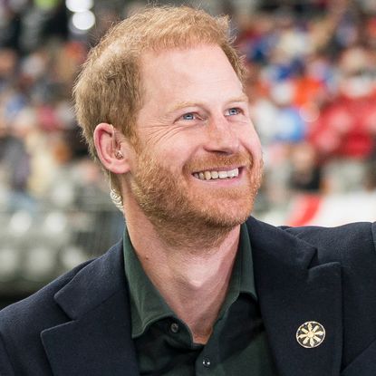 Prince Harry wearing a suit jacket and green shirt and looking up and smiling