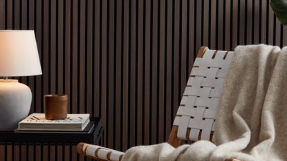 A slat panelled wall in dark wood with an accent chair and a side table in front of it