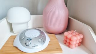 A Homedics white noise machine on a nightstand next to pink accessories