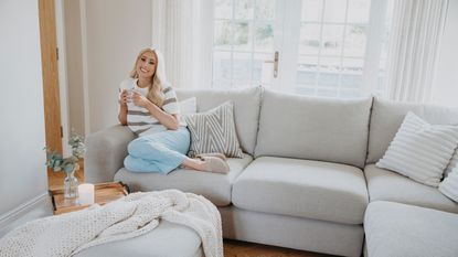 Stacey Solomon sitting on grey corner sofa with matching ottoman used as a coffee table