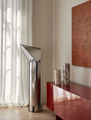 A corner of a living room with cream walls, and a red console