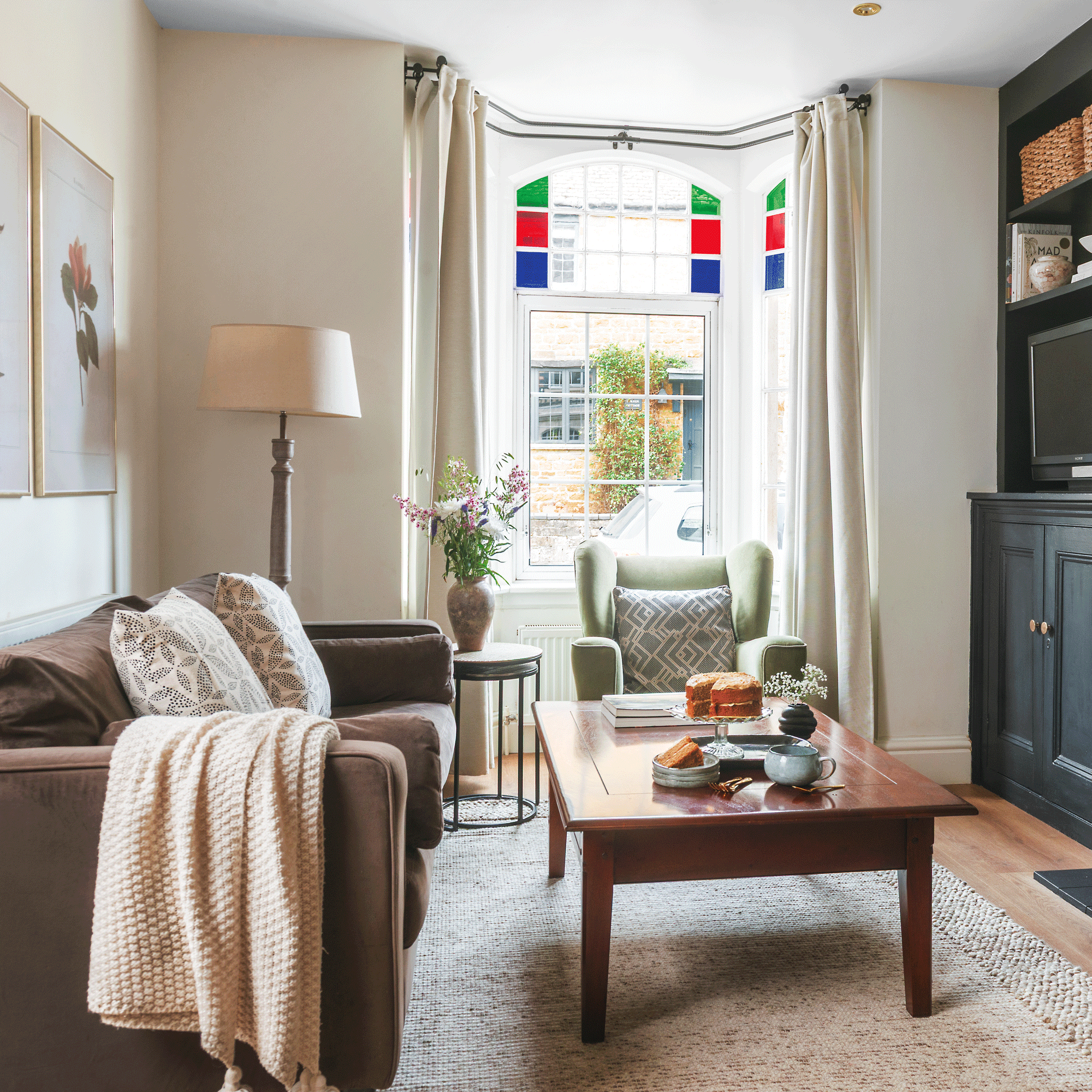a living room with stained glass windows a green armchair and a brown sofa, black alcove shelving and a wooden coffee table