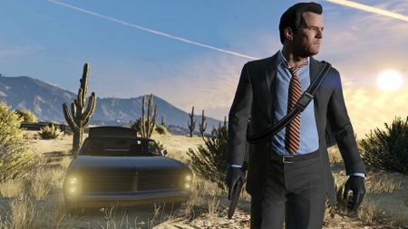 Michael from GTA 5 wearing a grey suit and walking outside in the desert with a car behind him.