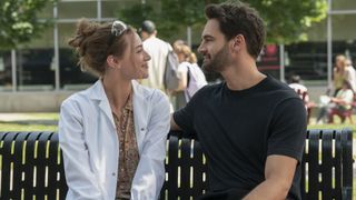 Lili Reinhart and Tom Bateman smile at each other on a bench in The Love Hypothesis