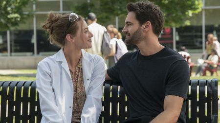 Lili Reinhart and Tom Bateman smile at each other on a bench in The Love Hypothesis