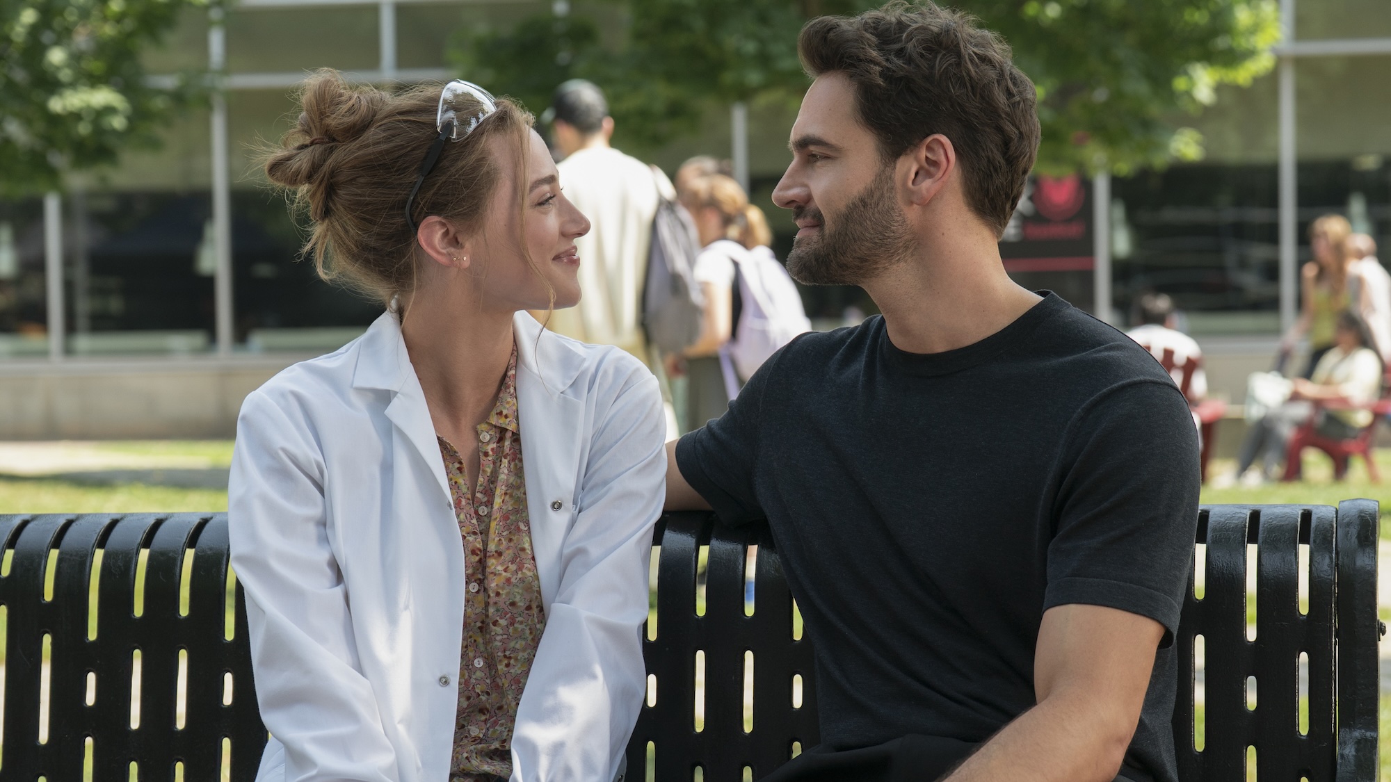 Lili Reinhart and Tom Bateman smile at each other on a bench in The Love Hypothesis