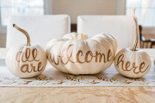 White pumpkins with lettering on a table, dining chairs in background