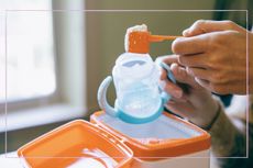 a close up of a hand putting baby formula into a baby cup