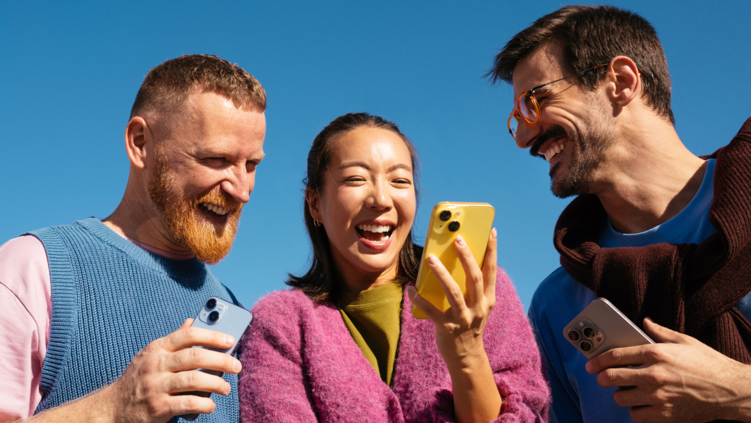 Three friends laugh as they look at a smartphone