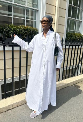 a woman's outfit showing what to wear in 80-degree weather with a white maxi shirt dress styled with a white mesh ballet flats styled with a black shoulder bag, black sunglasses, and a printed kerchief scarf