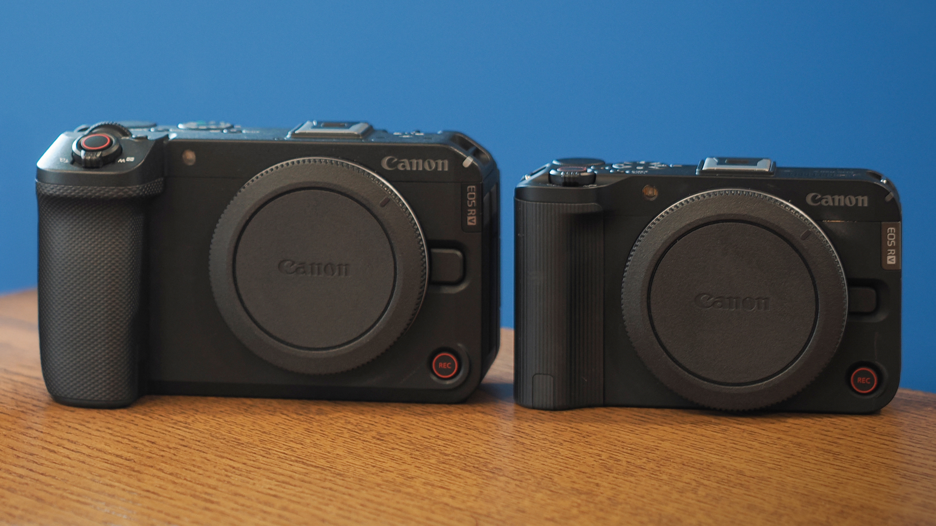 Canon EOS R50 V next to an EOS R6V on a wooden table in front of a blue background
