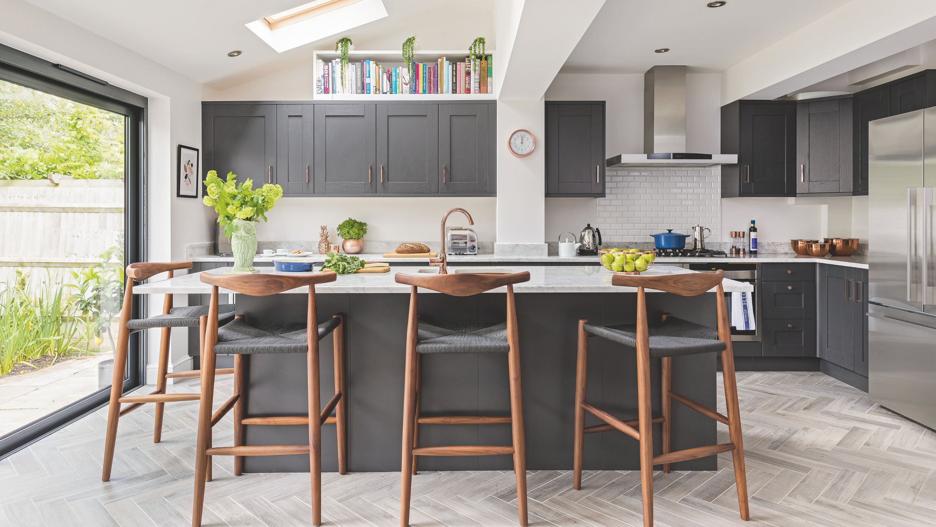 Open plan kitchen with white painted walls, and dark blue painted cabinets with a large island in the same colours in the middle. There are wooden bar stools around it too