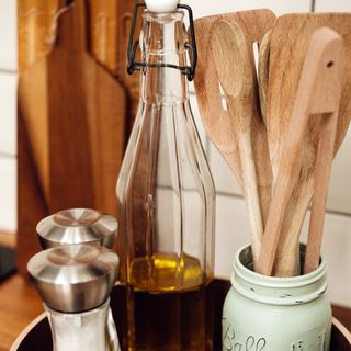 Assortment of wooden utensils in vase on kitchen counter next to glass bottle