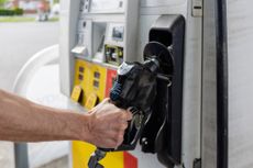 A man takes the gas pump from its dock in order to fill his tank with gas.