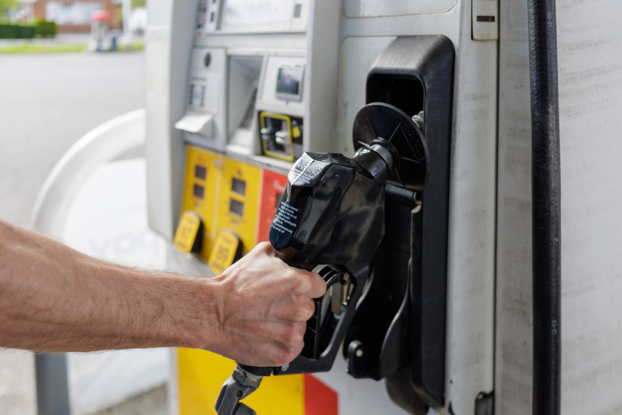 A man takes the gas pump from its dock in order to fill his tank with gas.