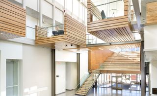 Inside The Taylor Institute of Teaching and Learning at the University of Calgary. We see a bright atrium, with "hanging pods" that are suspended by steel cables and serve as spaces for studying on the second floor, which we get to via wide staircase..