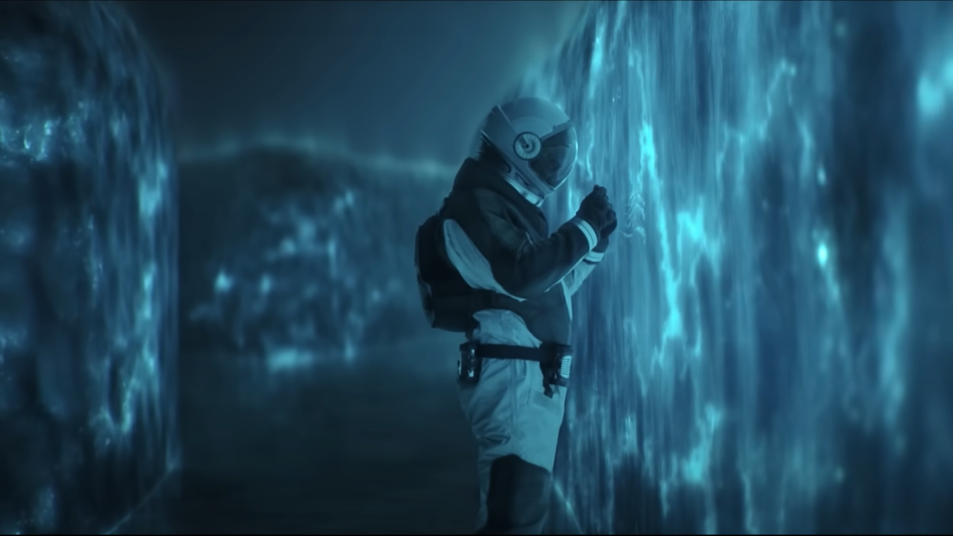 a man in a HAZMAT suit touches a shimmery blue wall