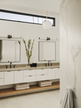 white bathroom with double vanity, double sinks and mirrors, shelf under the vanity, stone floor
