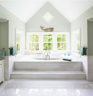 sunken bath in grand marble bathroom by large window