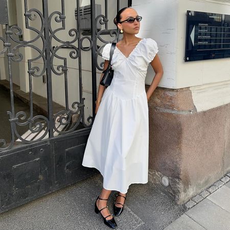 Ingrid wearing a white dress, black sunglasses, black handbag, and black mary janes.