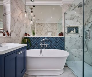 bathroom with large format marble effect tiles, blue tiles behind freestanding bath, large shower enclosure and blue vanity unit with sink