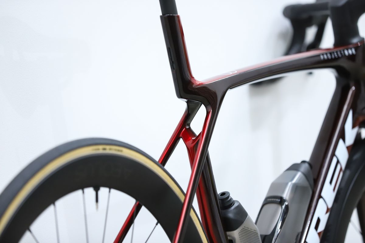 A red Trek Madone SLR 7 (gen 8) stands against a white wall