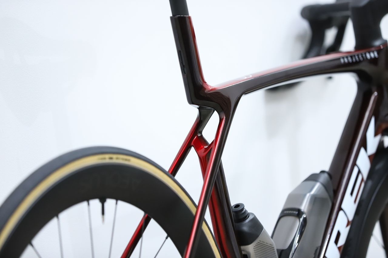 A red Trek Madone SLR 7 (gen 8) stands against a white wall
