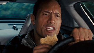 Dwayne Johnson eats a cookie while driving a fancy car in The Game Plan